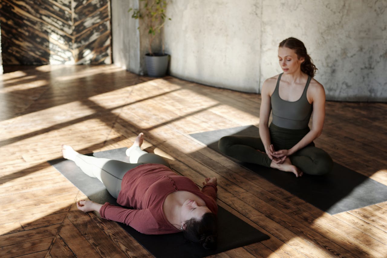 menu-10 Two women practicing yoga indoors with sunlight streaming in, highlighting focus and relaxation.