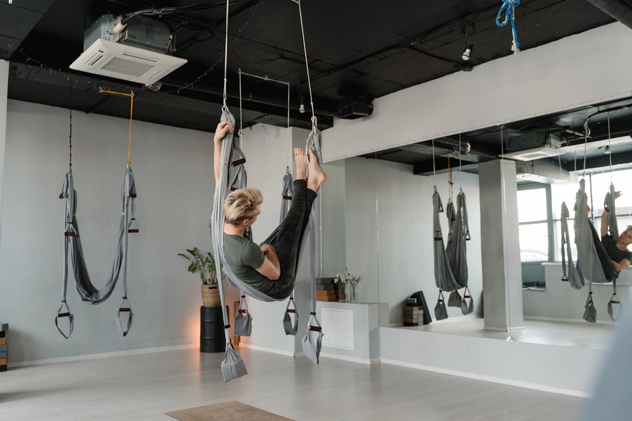 menu-18 Person practicing aerial yoga in a modern studio with mirrors and hanging fabric equipment.