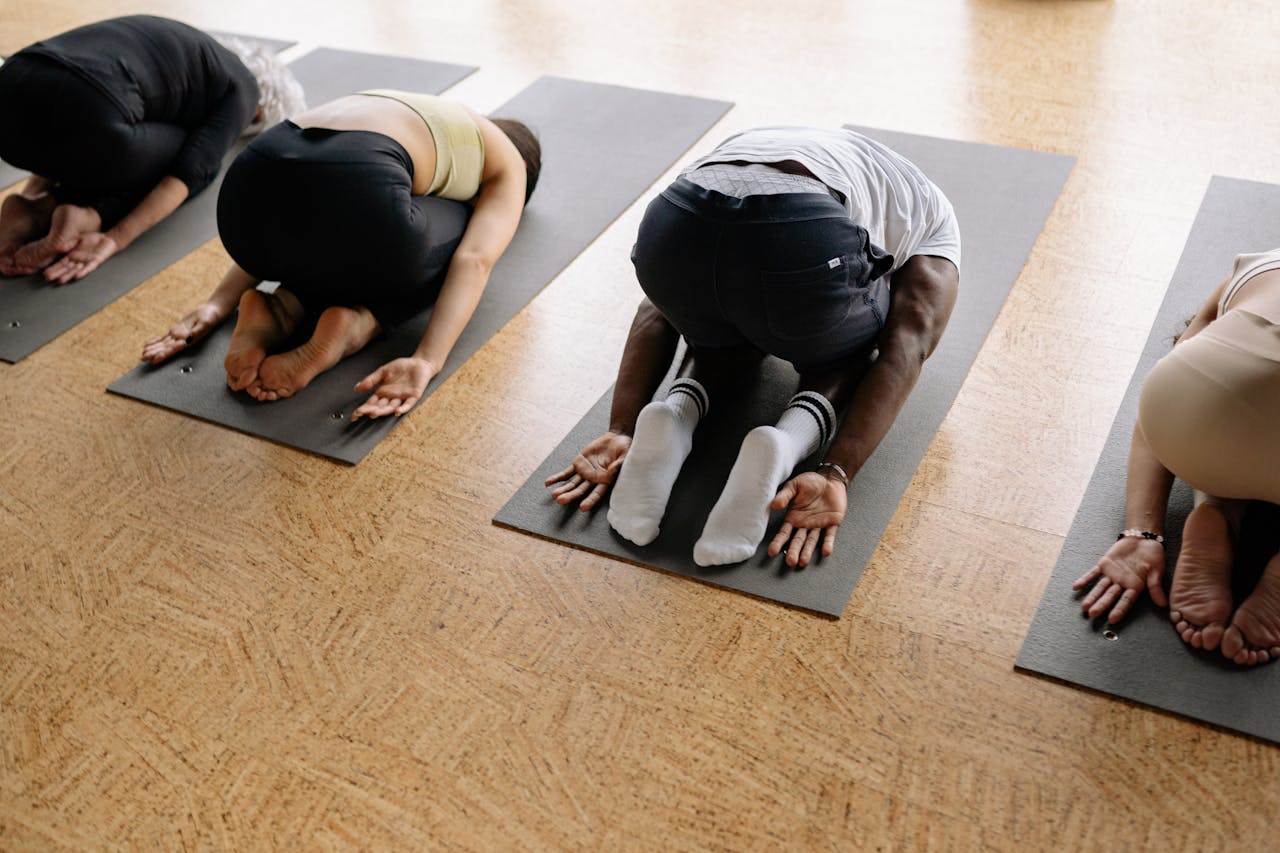 A group of people performing yoga exercises on mats in a studio setting, focusing on wellness and fitness.