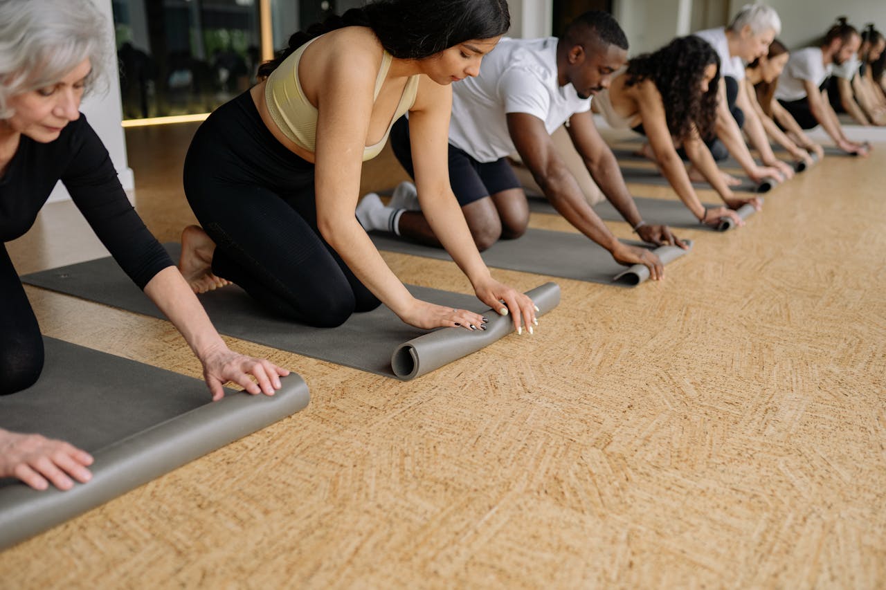 menu-08 A diverse group of adults rolling yoga mats in a studio before practice, promoting fitness and wellbeing.